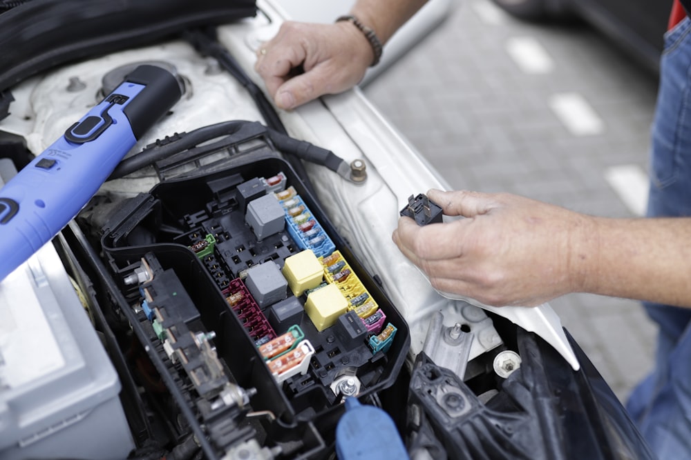 Gloved hands testing wiring inside a vehicle fuse box