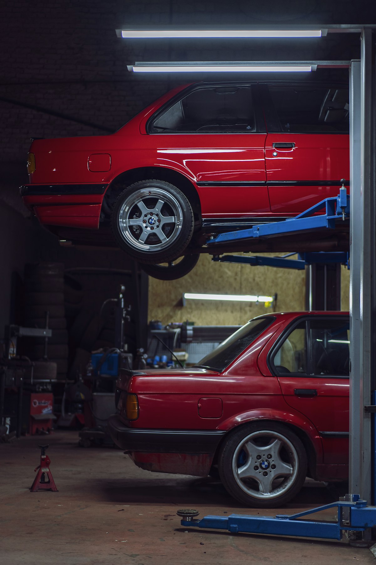 A red car raised on a two-post lift inside a repair bay
