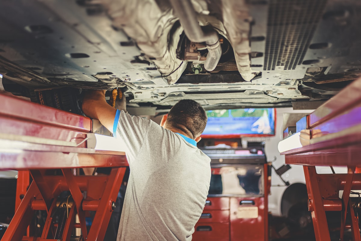 A technician's hands inspecting brake components under a vehicle on a lift